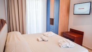 A hotel room with a bed, a TV displaying "WELCOME", and a wooden bench. - Dias studios (Apokoronas)