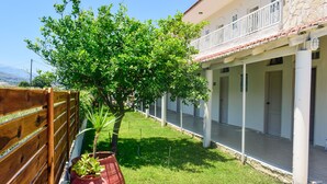 A courtyard with a wooden fence, potted plants, a tree, and a building with a balcony. - Dias studios (Apokoronas)
