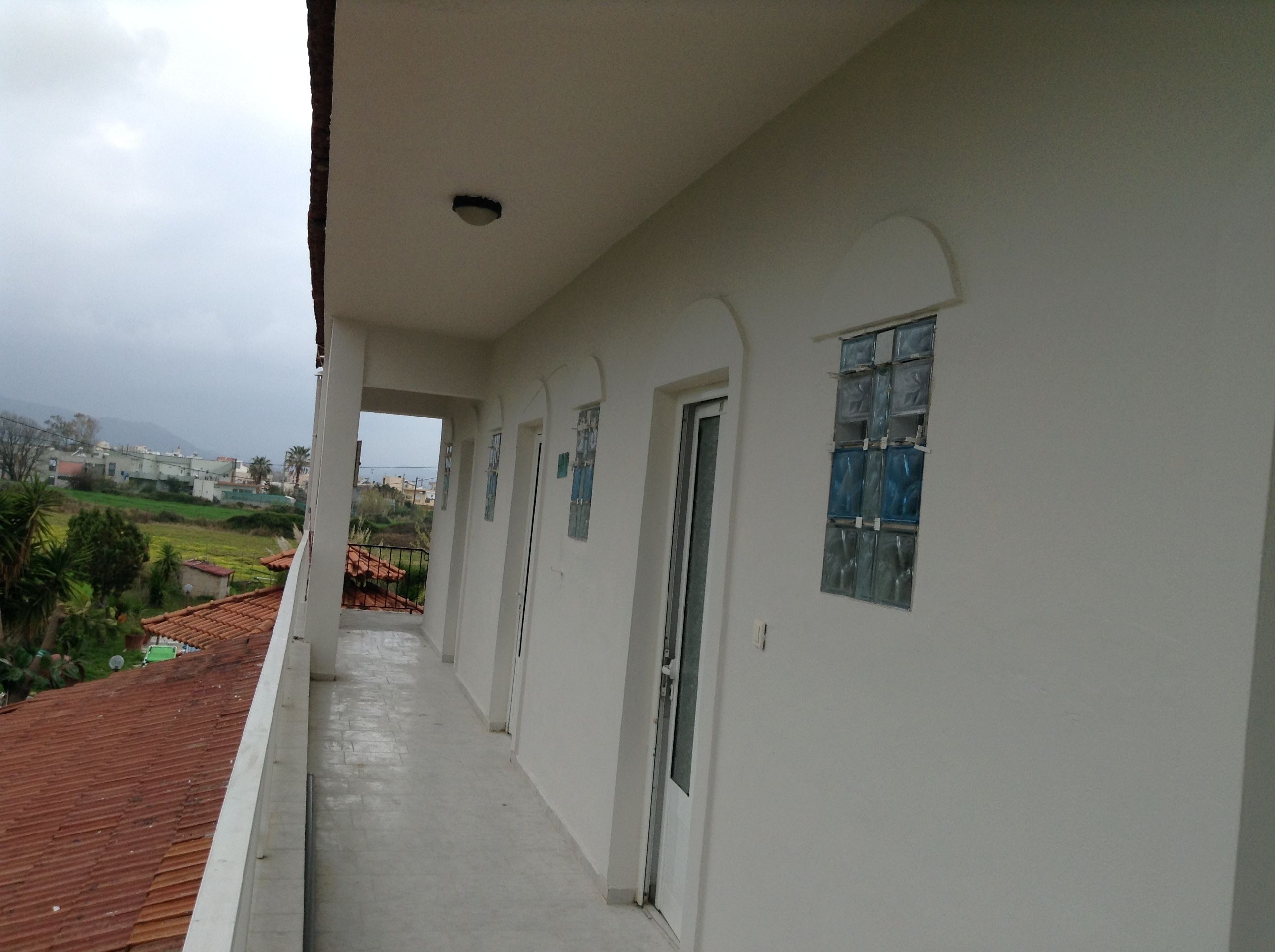 A corridor with white walls, a tiled roof, and a view of a green landscape.