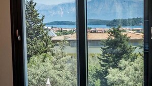 A room with a large window offering a view of mountains and a lake. There is a round table with a bottle of champagne and two glasses.