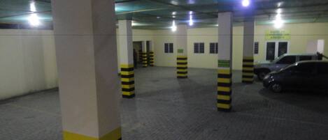 Un estacionamiento interior con pilares a rayas, suelo de baldosas y varios coches aparcados.