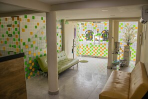 Un área de recepción con un sofá verde, uno beige y una pared de azulejos con cuadrados verdes, amarillos y blancos.