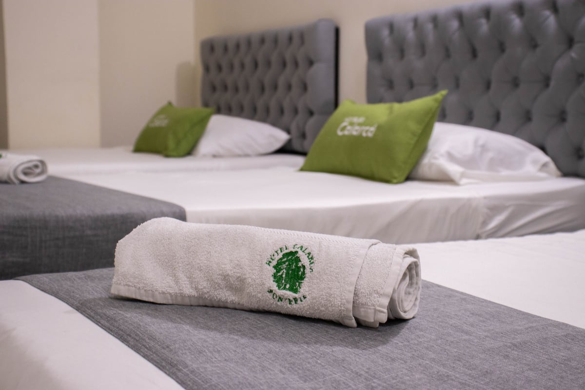 A hotel room with two beds, grey headboards, and a rolled towel on the bed.