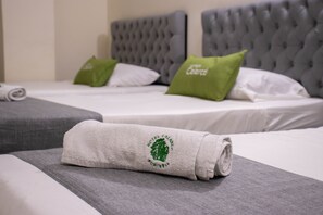 Habitación de hotel con dos camas, cabeceros grises y una toalla enrollada sobre la cama.