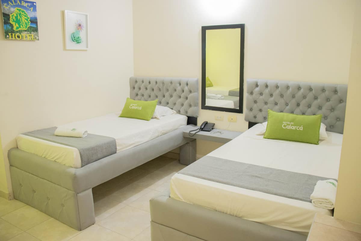 A hotel room with two beds, each with a grey headboard and a green pillow. There is a bedside table with a phone and a mirror on the wall.