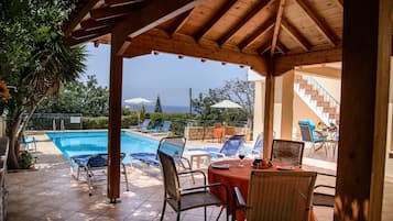 A covered outdoor area with a pool, lounge chairs, and a table with drinks.