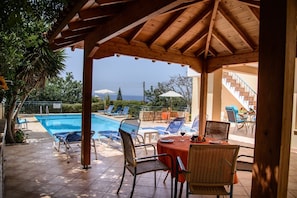 A covered outdoor area with a pool, lounge chairs, and a table with drinks. - Coral Sun Villas (Pegeia)