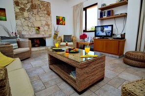 A living room with a stone wall, wicker furniture, a fireplace, and a television.