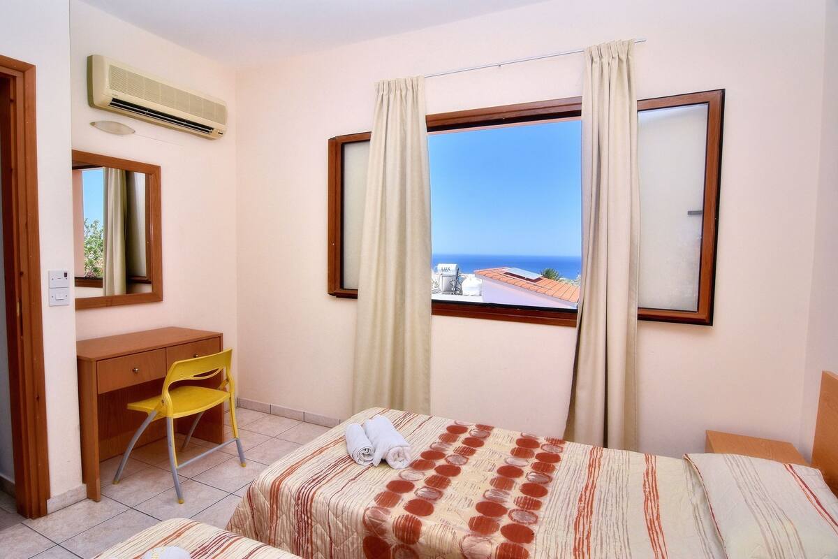 A hotel room with a bed, a desk, a chair, and a window with a view of the sea.