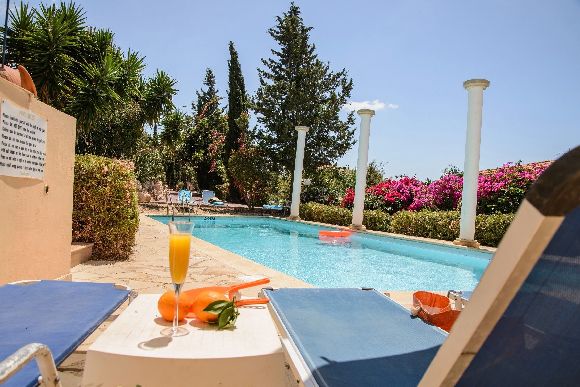 A poolside area with lounge chairs, a glass of orange juice, and a pool.