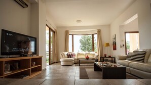 Sala de estar com televisão, sofás, mesa de centro e estante de livros.