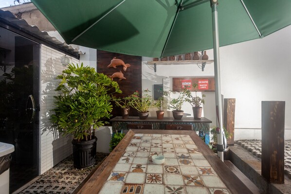 A tiled patio with potted plants, a wooden bench, and a green umbrella.