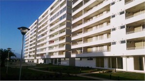 A multi-story hotel with balconies, a well-maintained lawn, and a street lamp. - Departamento Los Lucumos (La Serena)