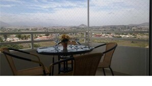 A balcony with a table and chairs, overlooking a cityscape with buildings and mountains. - Departamento Los Lucumos (La Serena)