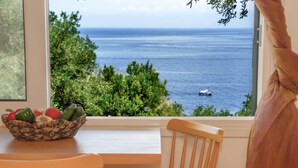 Un coin repas avec vue sur la mer, une chaise en bois, une table et un panier de légumes.