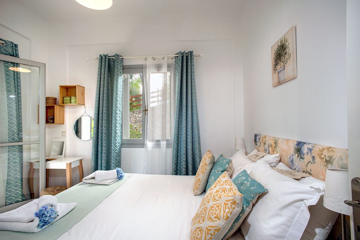 A bedroom with a bed, a desk, a chair, a mirror, and a window with curtains.