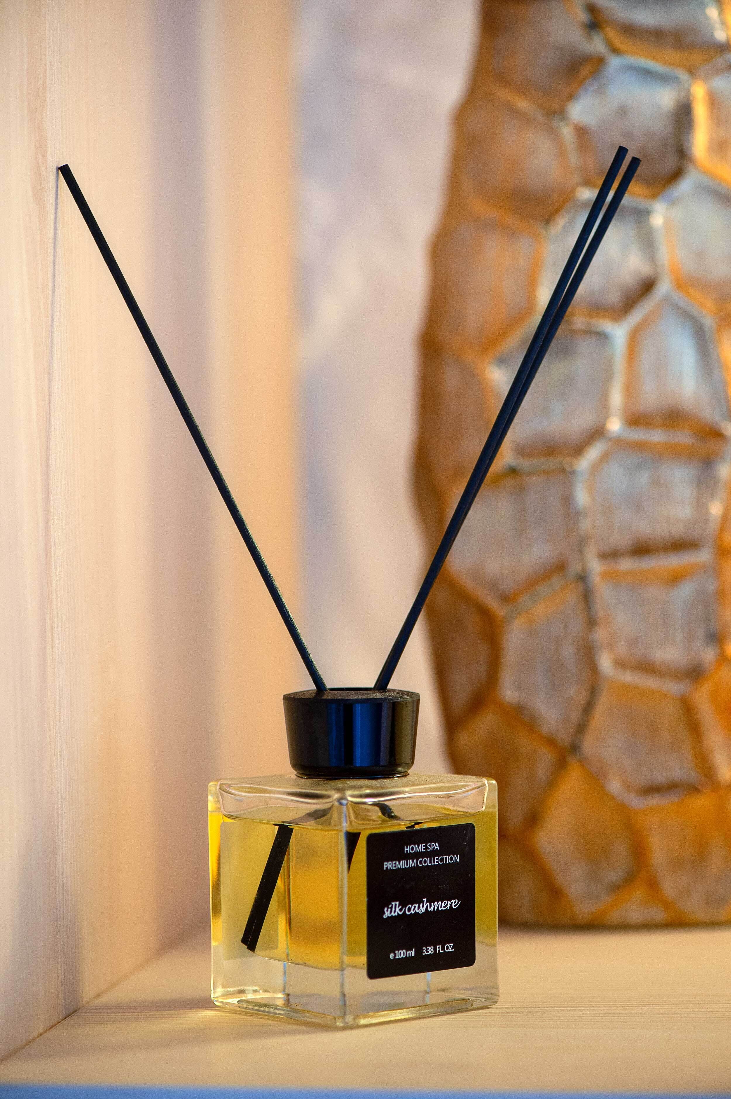 Een fles Silk Cashmere eau de cologne met twee zwarte rieten stokjes, voorzien van de tekst 