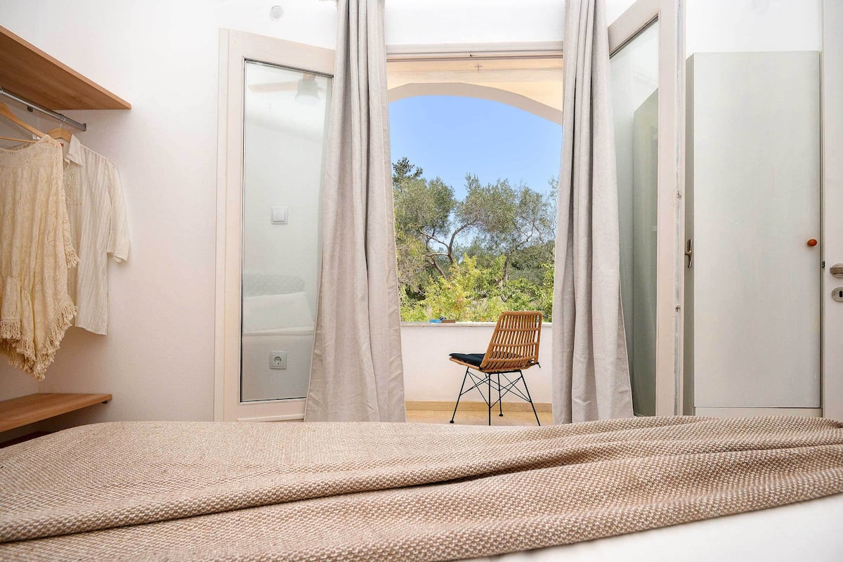 A bedroom with a bed, a chair, and a view through an open door.