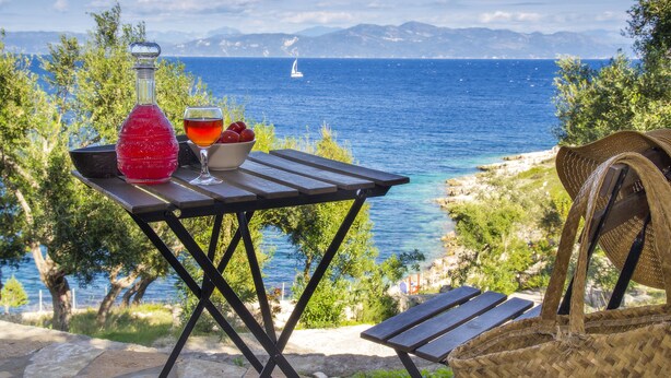Une table avec une bouteille, un verre et un bol de fruits, le tout placé devant un paysage côtier pittoresque.