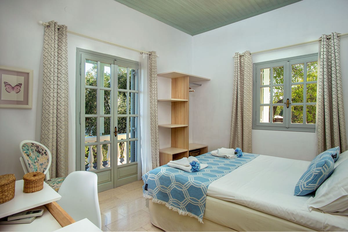 A bedroom with a bed, a chair, a table, and a window.