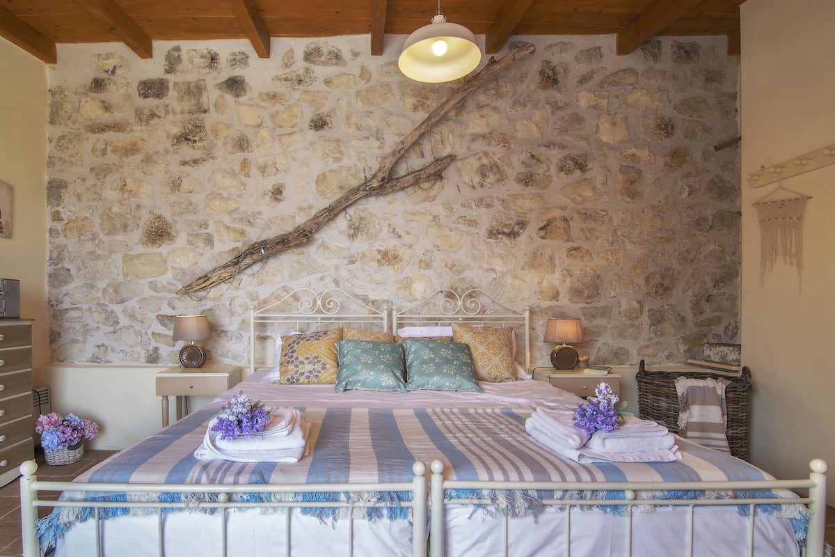 A bedroom with a stone wall, a bed with a headboard, two bedside tables with lamps, and a hanging light fixture.