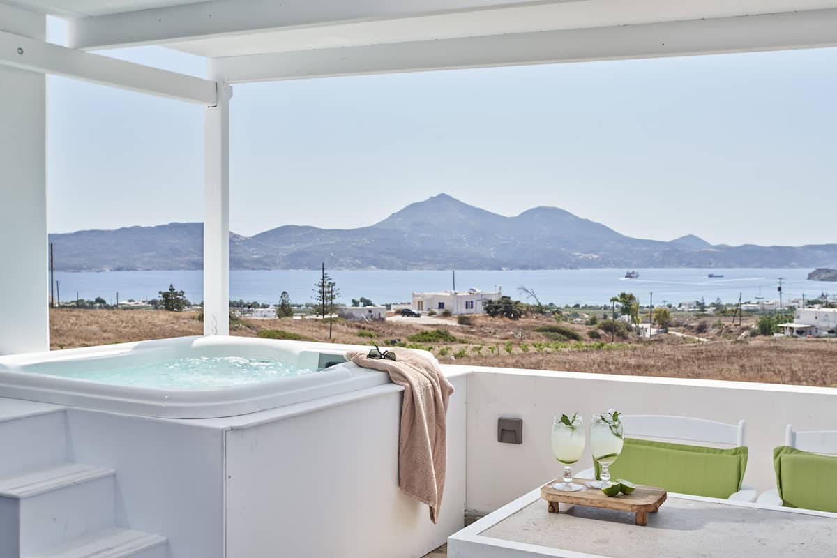 A hot tub with a towel, a table with glasses, and a view of the sea and mountains.