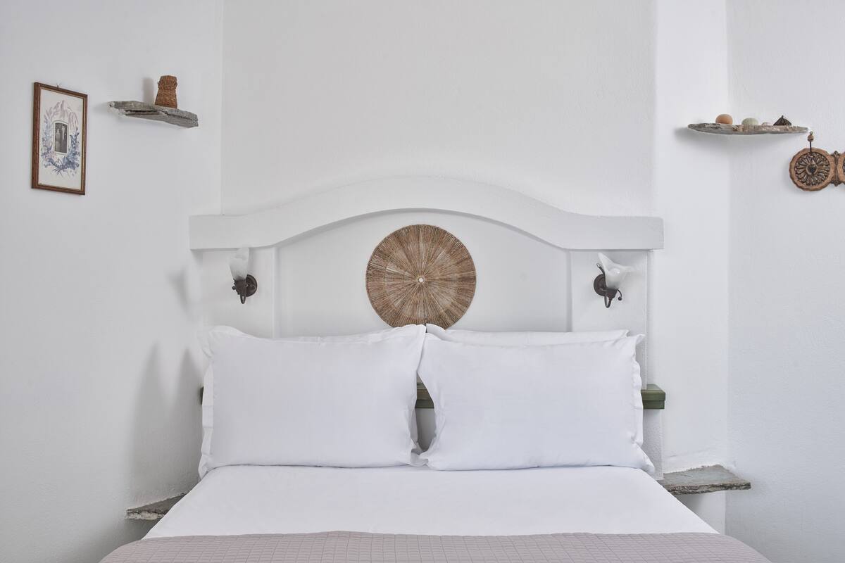A bed with white bedding, a round woven headboard, and two wall-mounted sconces.