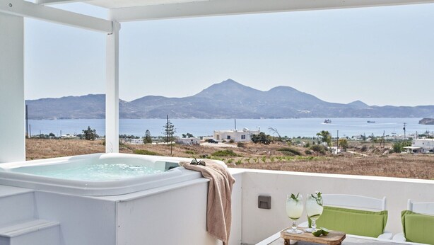 Een jacuzzi met een handdoek, een tafel met glazen en uitzicht op zee en bergen.