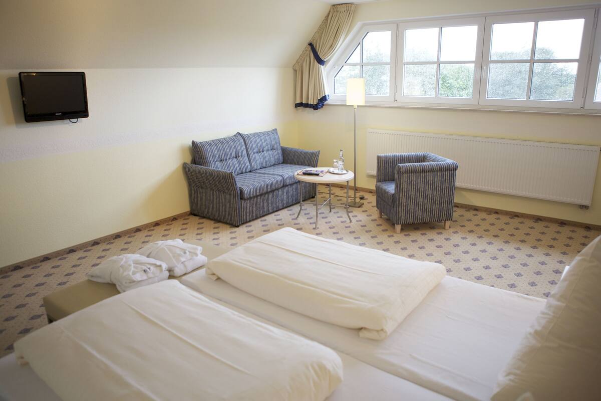 Une chambre d’hôtel avec un canapé, un fauteuil et deux lits.
