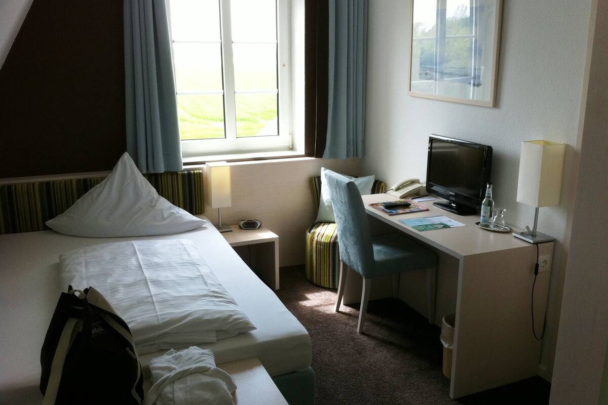 Une chambre d’hôtel comprenant un lit, un bureau avec un ordinateur, une chaise, un téléphone et une fenêtre avec des rideaux.