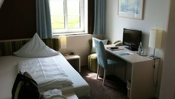 A hotel room with a bed, a desk with a computer, a chair, a telephone, and a window with curtains.