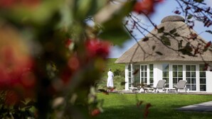 A thatched-roof building with a glass enclosure, a lawn, and a person in a white robe. - Lundenbergsand Hotel und Spa (Simonsberg)