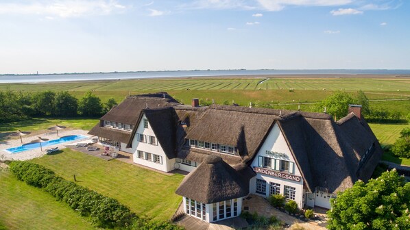 A large, thatched-roof hotel with multiple guest rooms, a swimming pool, and expansive views of the surrounding countryside. - Lundenbergsand Hotel und Spa (Simonsberg)