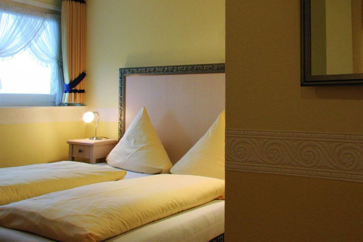 Une chambre d’hôtel avec deux lits, une table de chevet avec une lampe, une fenêtre avec des rideaux et un miroir au mur.