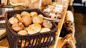 A buffet table with baskets of bread and pastries, a coffee station, and potted plants. - Lundenbergsand Hotel und Spa (Simonsberg)