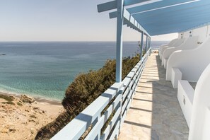 A seaside hotel with a covered walkway, white chairs, and a view of the ocean. - Thalassopetra (Milos)