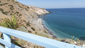 A coastal landscape with a clear view of the sea, a sandy beach, and a rocky hillside. - Thalassopetra (Milos)