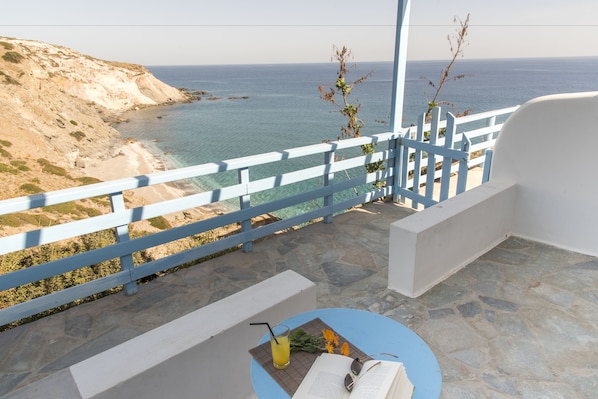 A balcony with a view of the sea, a table with a book and a drink, and a white railing.