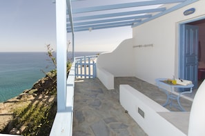 A coastal balcony with a stone floor, white walls, and a blue door.