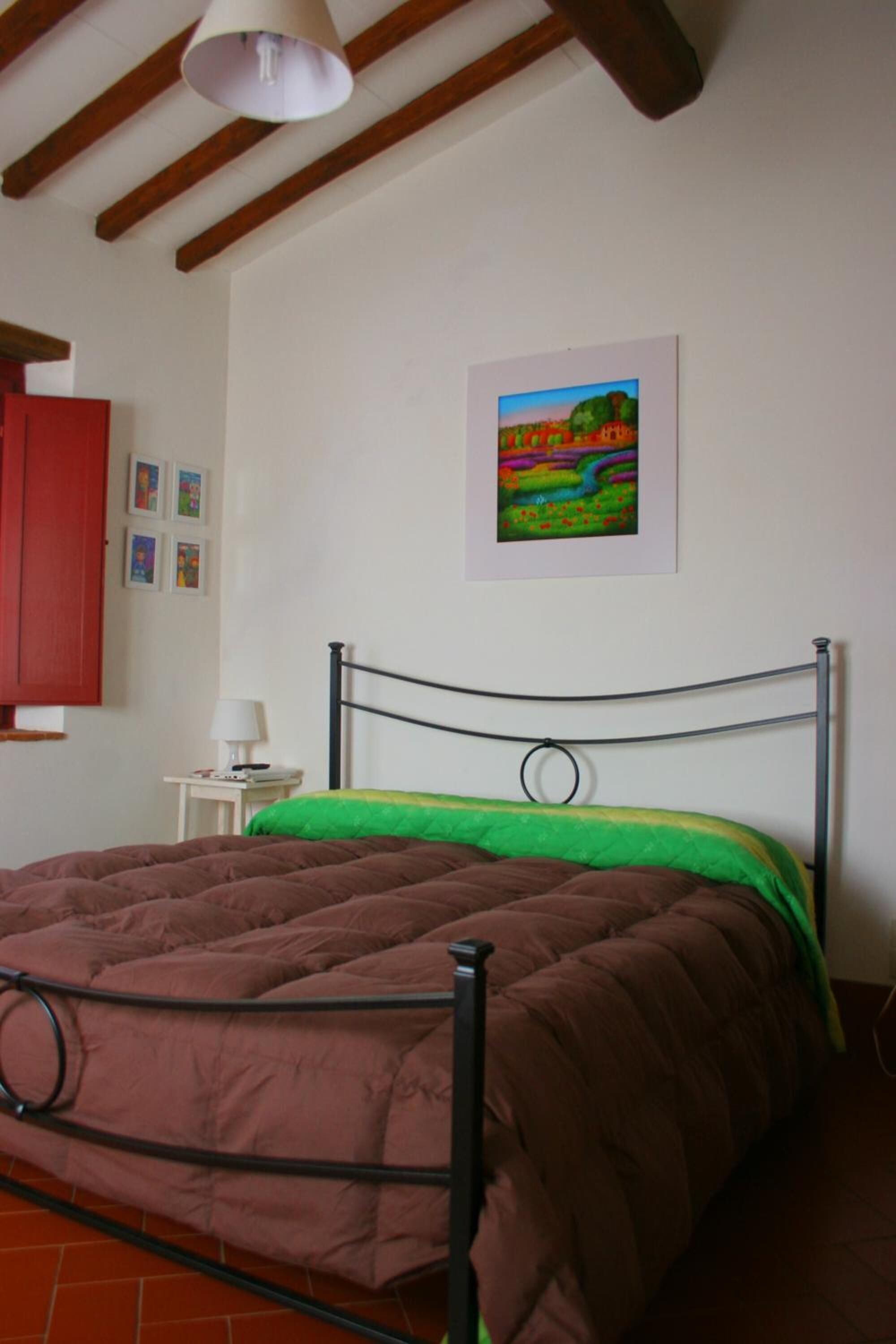 Une chambre à coucher avec un lit en métal, une couvre-lit verte et marron, une armoire rouge et un tableau représentant un paysage accroché au mur.