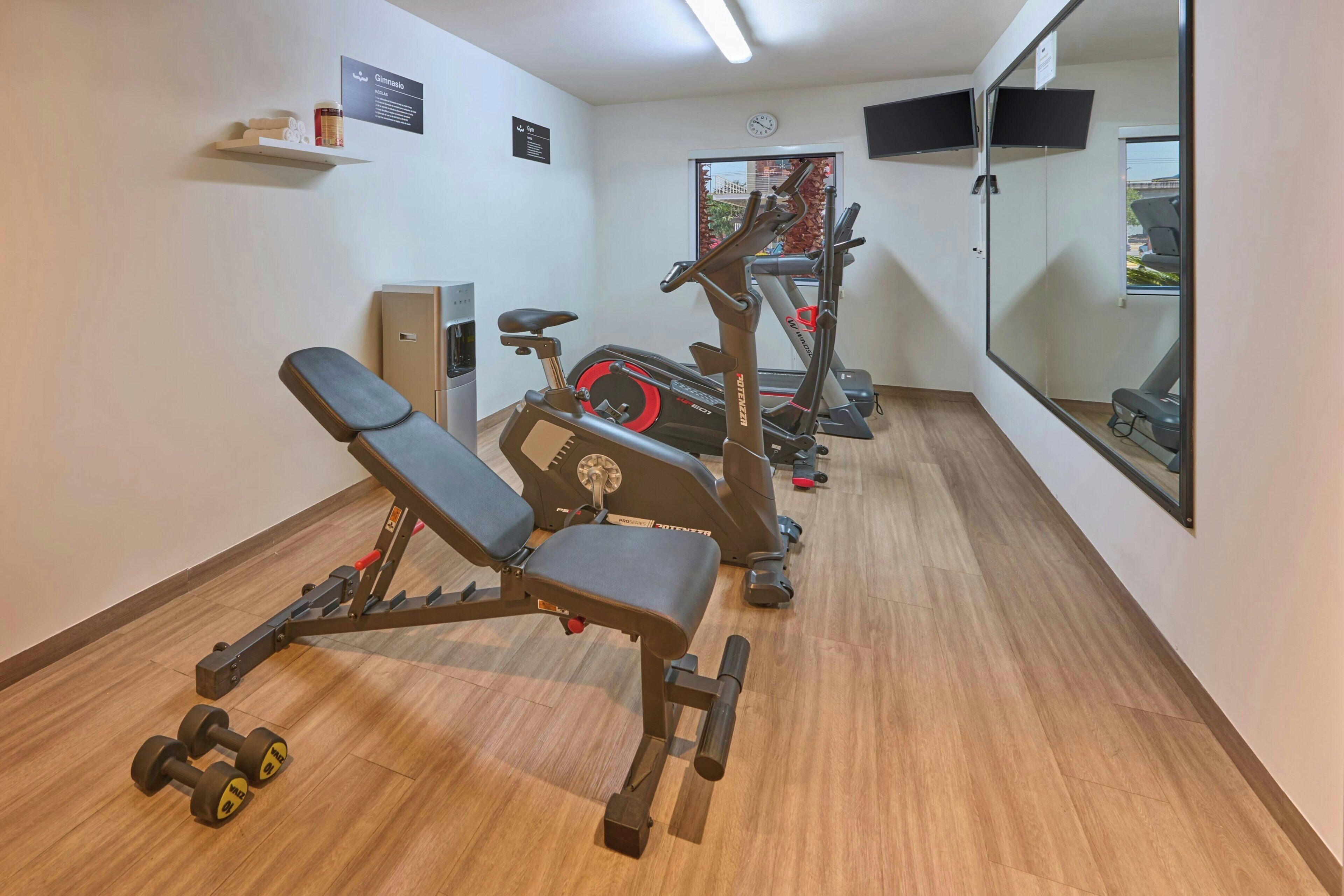 Uma academia com equipamentos de exercício, um banco e um espelho.