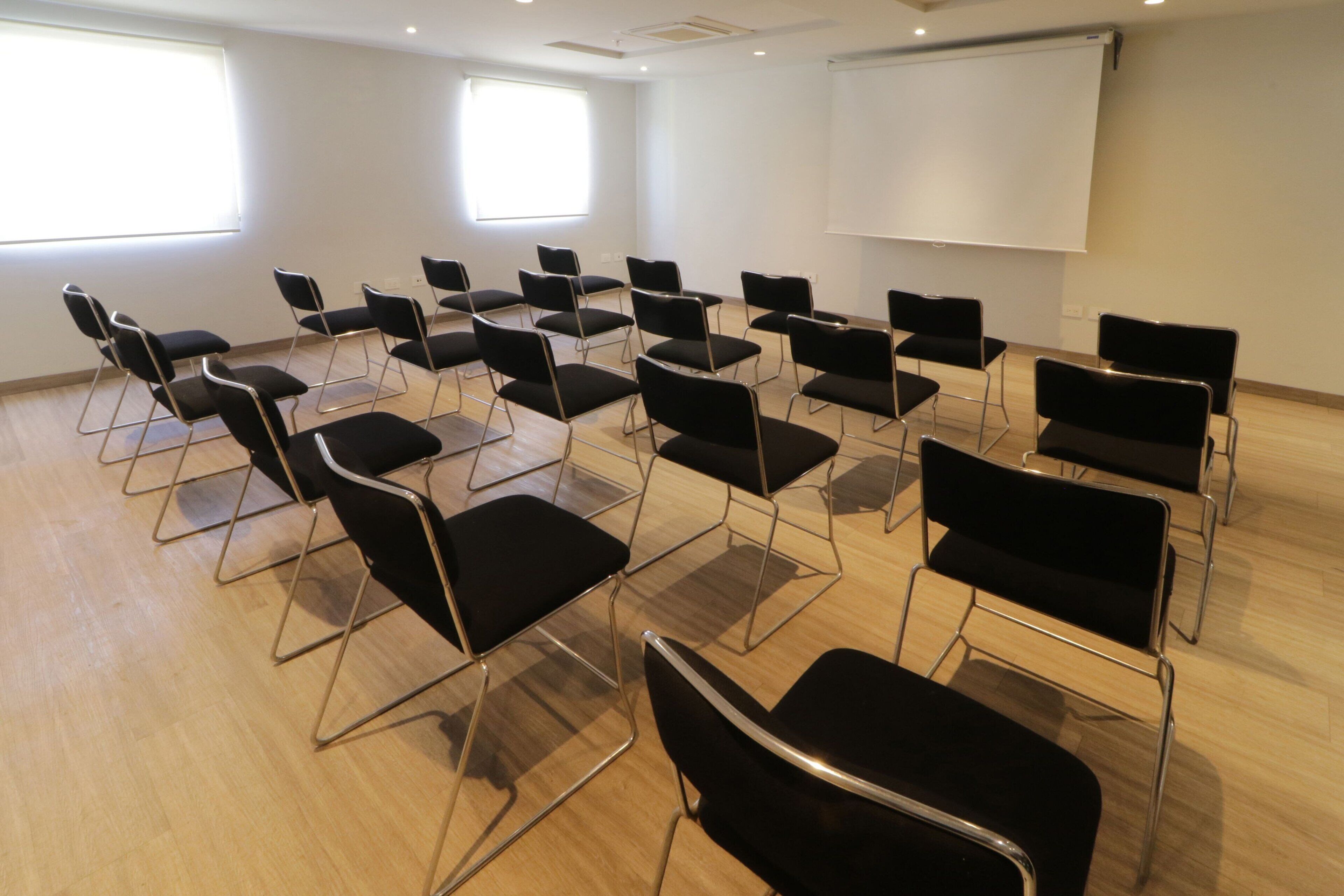 Une salle de conférence avec des rangées de chaises noires et un tableau blanc.