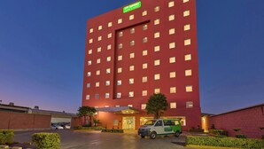 Um hotel de vários andares com fachada vermelha e um letreiro verde indicando que pertence à rede City Express.