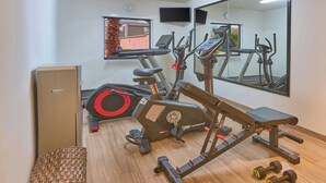 Academia com equipamentos de exercícios, um banco, um espelho e uma cesta de vime.