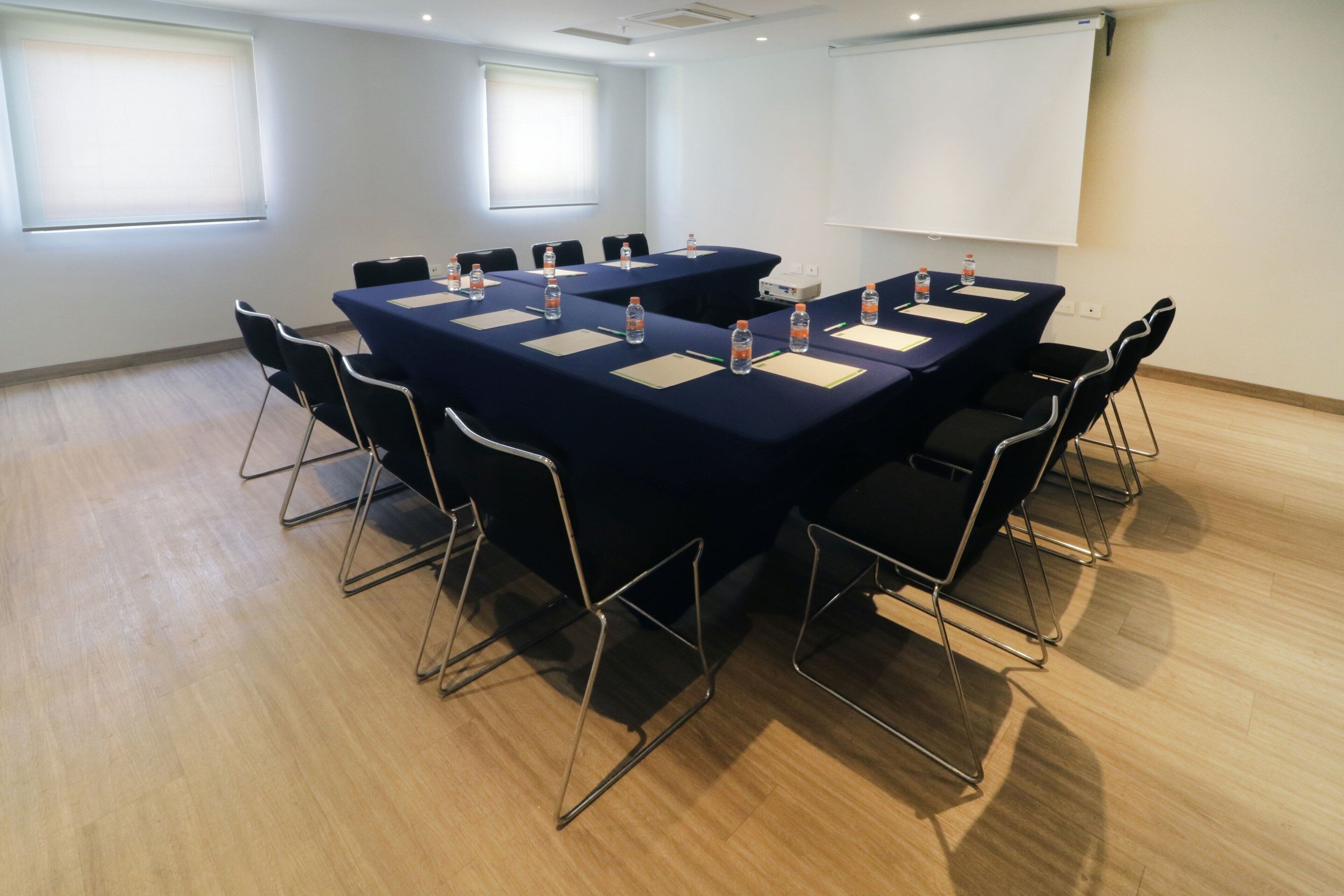 A conference room with a large table, chairs, water bottles, and a projector screen.
