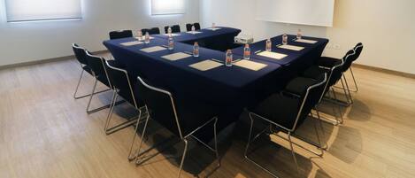 A conference room with a large table, chairs, water bottles, and a projector screen.
