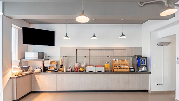 Cozinha moderna com televisão de tela plana, luminárias pendentes, máquina de café e exposição de frutas.