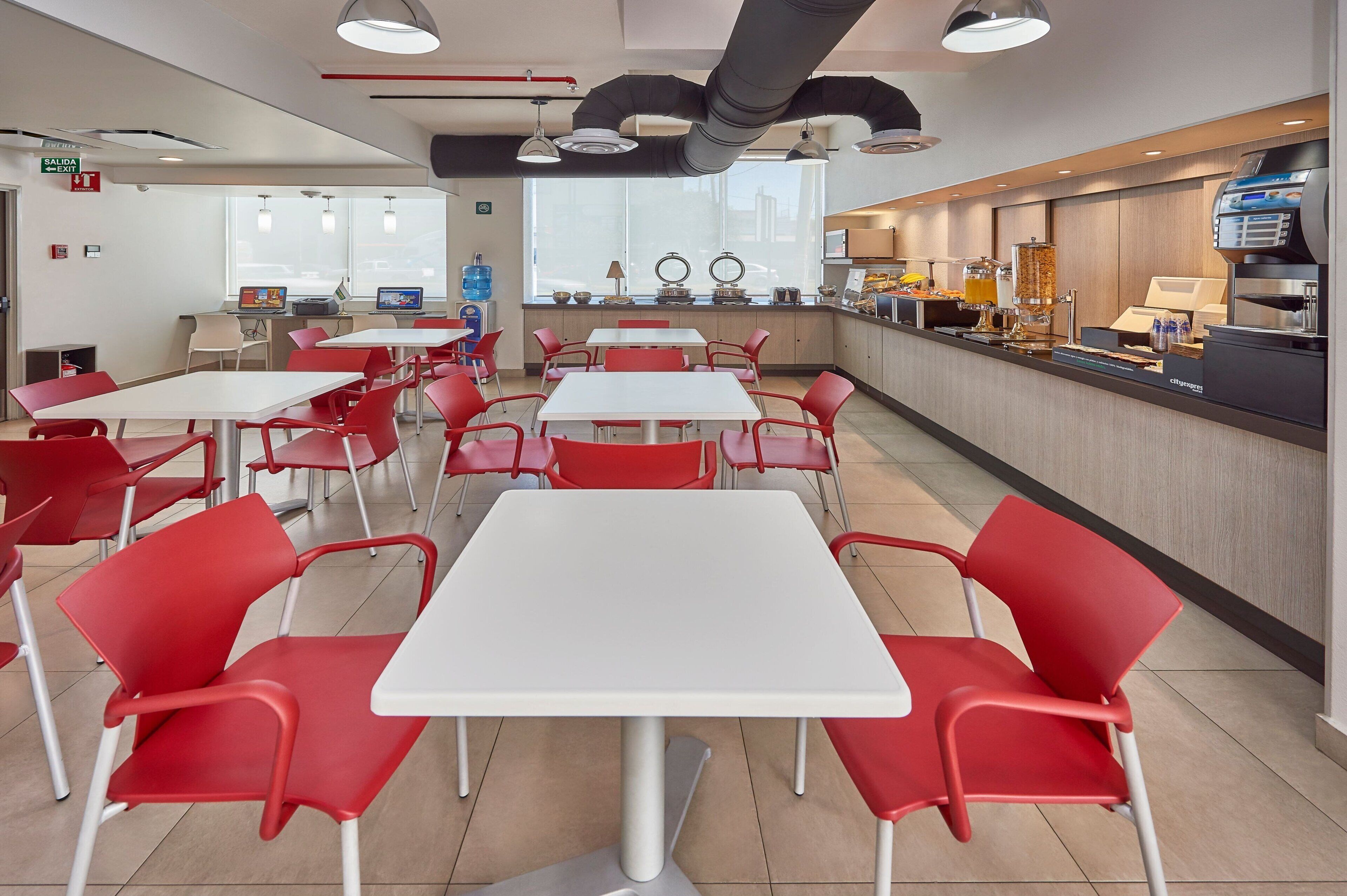A modern cafeteria with red chairs and white tables, a coffee machine, and a water dispenser.