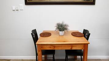 Uma mesa de jantar com quatro cadeiras, um vaso de planta e um quadro com paisagem na parede.