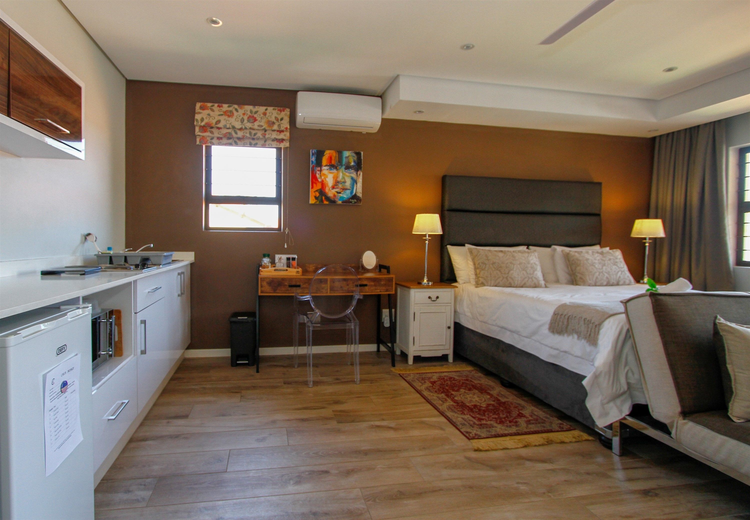A hotel room with a bed, bedside lamps, a desk with a chair, a small cabinet, and a window with a floral curtain.